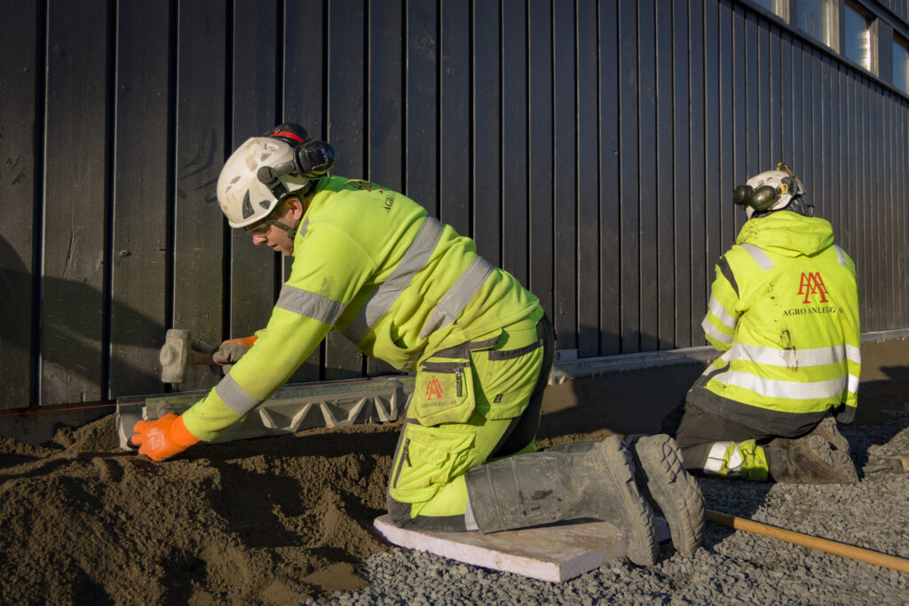 To anleggsarbeidere plasserer Ulefos rennesystem langs vegg. Foto.