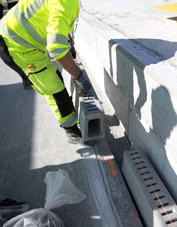 Anleggsarbeider plasserer Ulefos Filcoten dreneringsrenne langs betongkant. Foto.